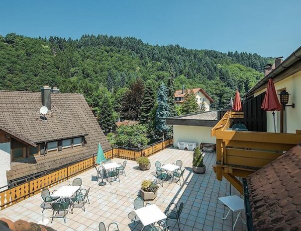 Sonnige Hotelterrasse mit Sitzplätzen, Blick auf grüne Wälder und umliegende Häuser, ruhige Lage in der Natur, ideal für Erholung und Urlaub in Deutschland
