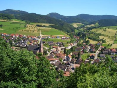 Panoramablick auf idyllisches Dorf in den Bergen mit grünen Hügeln, Wäldern, Feldern und typischen Häusern, ländliche Landschaft in Süddeutschland, ideal für Natururlaub und Erholung