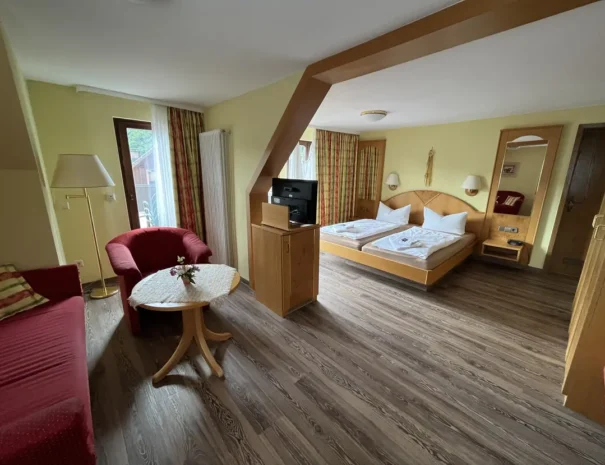 Helles Hotelzimmer mit Doppelbett, Sitzbereich, Holzboden, TV, Balkonzugang und gemütlicher Einrichtung in warmen Farben, ideal für Urlaub oder Kurzaufenthalt in Deutschland